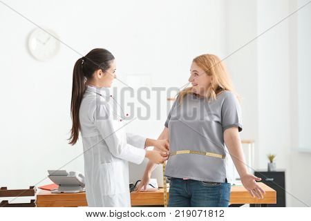 Young female doctor measuring waist of overweight woman with centimeter in clinic