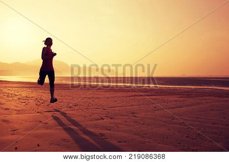 Young fitness woman running on sunrise sandy beach