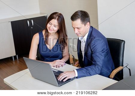 Business man explaining something to a woman with a laptop in an office.