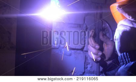 The process of manufacturing a decorative metal product. Metal sparks fly apart from the detail. Welding of metal in the process of creating decorative metal products worker supports orange mask hand.