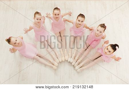 Little ballerinas in ballet studio, top view. Group of girls practicing position sitting on floor, classical dance studio