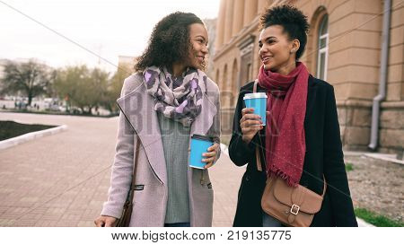 Two beautiful mixed race woman friends drink coffee and talking after shopping and walking city street