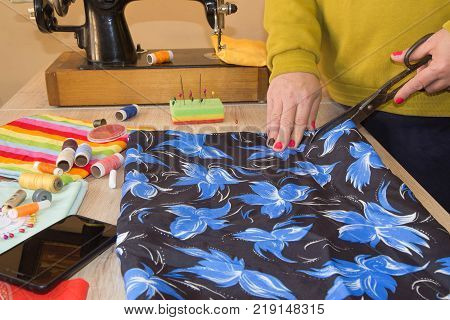 Couturier sews a dress in the studio. Fashion designer making a pattern on a red piece of tissue. Sewing machine is standing on the table beside them