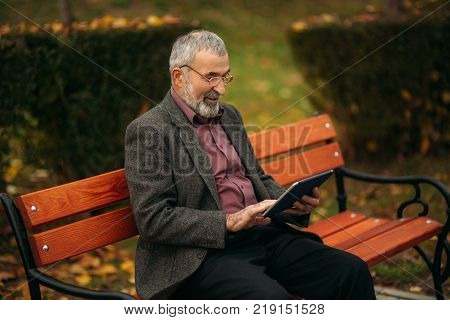 Grandpa use a tablet sitting in the pakr on the bench.