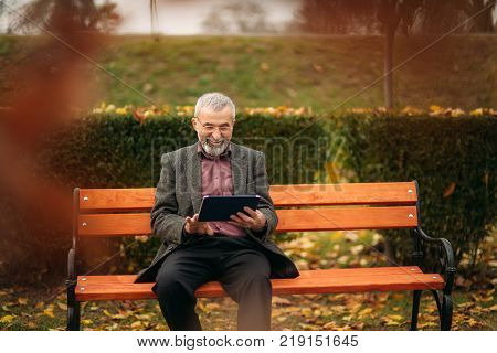 Grandpa use a tablet sitting in the pakr on the bench.