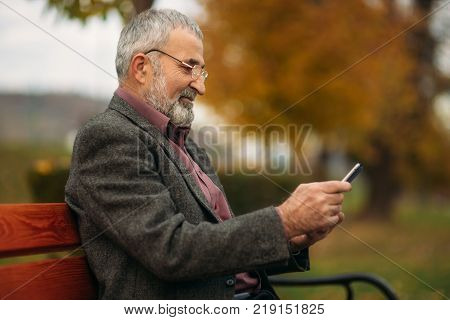 Grandpa use a tablet sitting in the pakr on the bench.