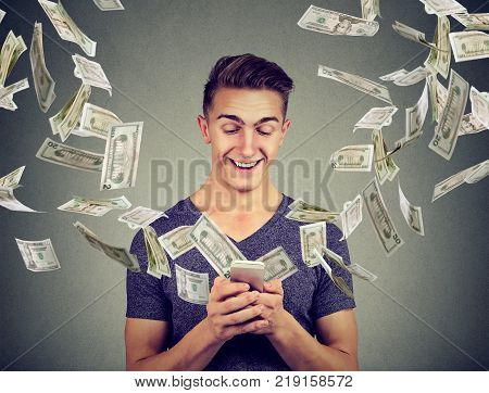 Online banking money transfer e-commerce concept. Young man using smartphone with dollar bills flying away from screen