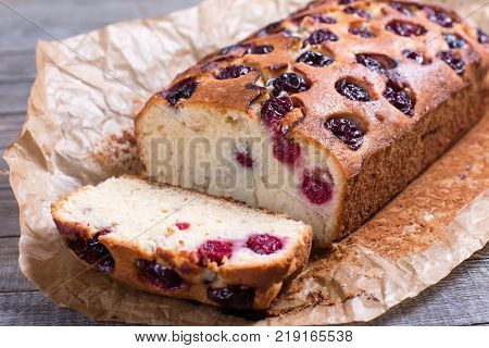 Slice of homemade cranberry cake with cherries on a wooden background