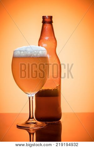 Bottle of beer and glass full foam condensate cold refreshing Still life on golden translucent background studio shot