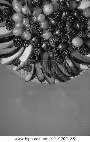 Fruit and berry platter with ripe fresh sweet vibrant healthy organic red raspberry peach blackberry green grapes and on round plate on blue background copy space