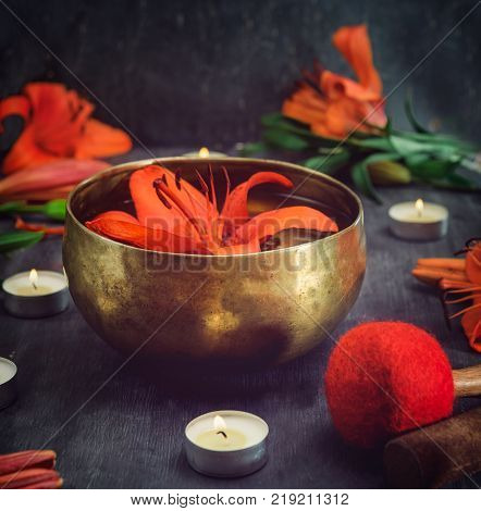Tibetan singing bowl with floating in water lily inside. Special sticks burning candles lily flowers and petals on the black wooden background. Meditation and Relax. Exotic massage. Selective focus