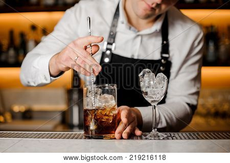 Bartender in a white shirt and apron pouring a portion of alcoholic drink into a metal cup