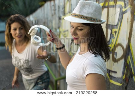 two adult girls sitting in the shade on the stairs listening to music and photographing with a tablet