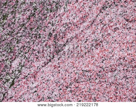 A close-up of a surface of treated rose granite rock plate. A fragment of a stone wall decoration. Texture of deep rose granite facing material.