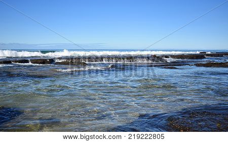 A wave crashing at the beach with rocks