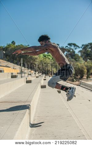 Muscular Jamaican athlete jumping high with plyometric workout at stadium steps.
