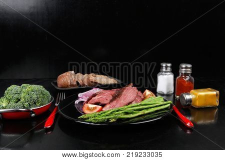 business lunch fresh roast beef meat slices on black plate wotj cutlery asparagus boiled broccoli rye bun on wooden table