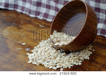 Oat spilling out from wooden bowl on wooden table