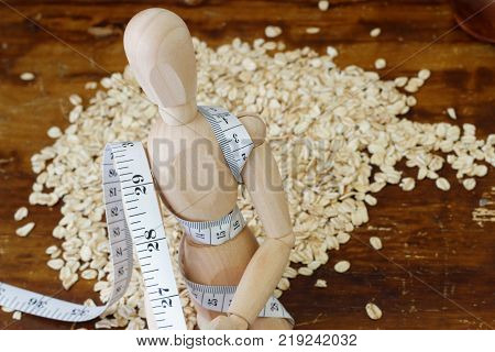 Wooden dummy is strapped with tape measure with pile of rolled oat in the background. Concept of weight loss and management