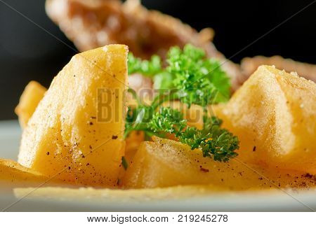 Little white bowl served with goldy fried potato slices, roasted sausage and decorated with green parsley leaves. Looks very delicious and nourisihing.