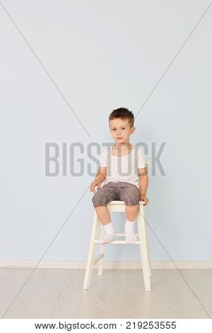 European teenage boy in a white shirt and blue shorts sitting on a chair with the tablet computer. Looking at the camera. Studio shot, isolated on white background.