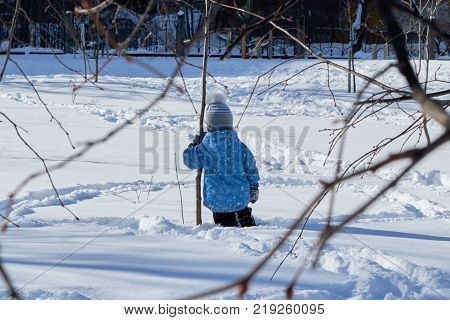 A boy stands knee-deep in the snow back to us and clings to the tree. He's upset and lonely. Child is sad and pining. In the foreground the branches of trees. Damaged relationships and resentment.