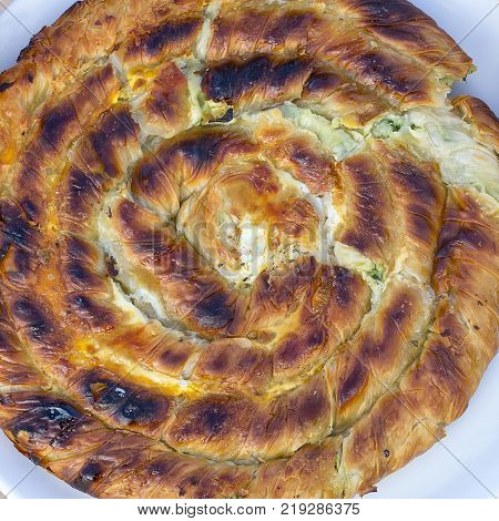 Round burek or pie in white plate, close up, top view. Turkey