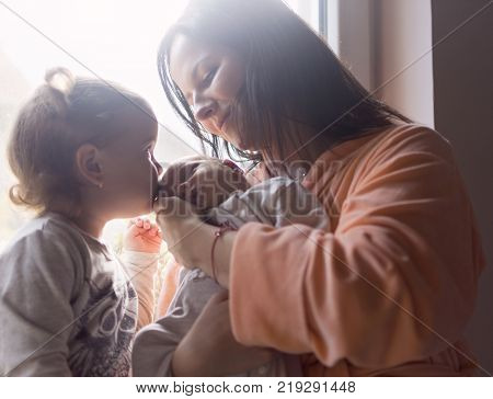 Mother and older daughter enjoy a new family member kissing him on the first morning sunshine