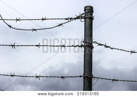 corroded barb wire with grey sky and clouds