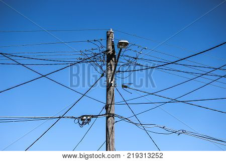 high voltage electricity pole with complex wiring, street lamp and blue sky