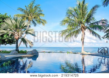 Morning time at swimming pool and the blue sea with palmcoconut trees with background white clouds and blue sky peacful and realax tropical resort in asia.