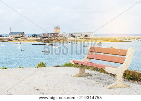 Empty bench in red metal and white cement install on the floor at sea side with background boat float on blue ocean and building behide white clouds sky.