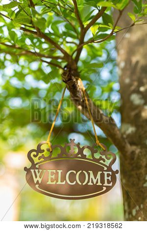 Metal welcome sign hang on tree with bokeh blurred background in the garden