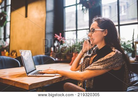 Beautiful Young Brunette Woman Inside Cafe With Christmas Interior At Wooden Table By The Window Tal