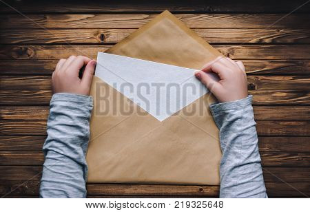A large brown envelope holds the child's hands. Open envelope on a wooden background. A blank sheet of paper in an envelope. Copy space.