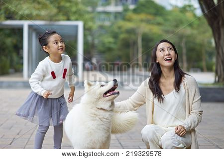 mother and daughter laughing & playing with dog outdoor in garden