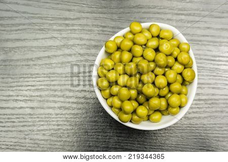 Green peas in a white bowl on the table. View from above