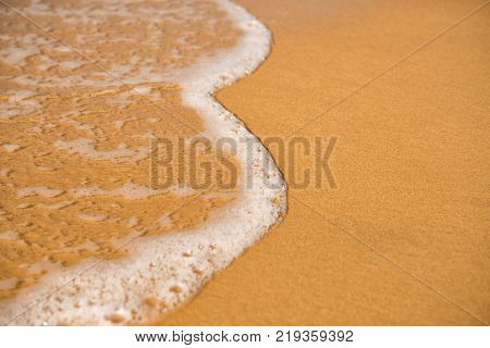 Background. A close-up of a wave runs over a sandy beach