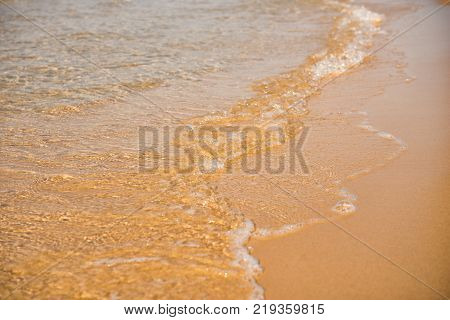 Background. A close-up of a wave runs over a sandy beach