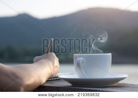 People writing and planning work on wooden balcony and cup of hot coffee for brackfast near river and mountain background