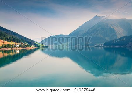 Sunny summer morning on Resia (Reschensee) lake. Curon Venosta village in the morning mist Province of Bolzano - South Tyro Italy Europe. Artistic style post processed photo.