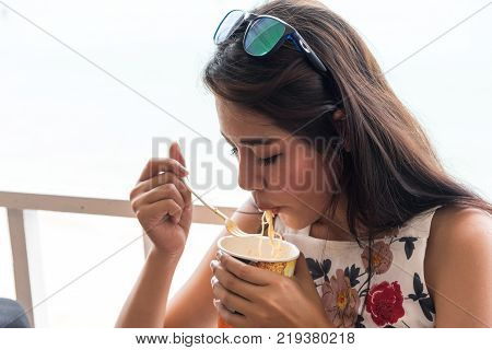 Asian young beautiful woman wearing sunglasses is eating hot noodles and spicy.