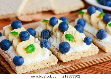 Crispbread toast with cottage cheese, banana and berries on wooden board. Cottage cheese open sandwich idea. Closeup