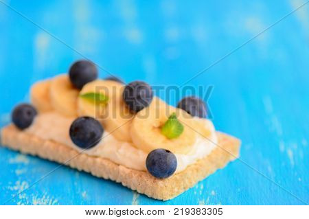 Crispbreads with sweet cottage cheese, fresh banana, berries and mint on blue wooden background. Closeup
