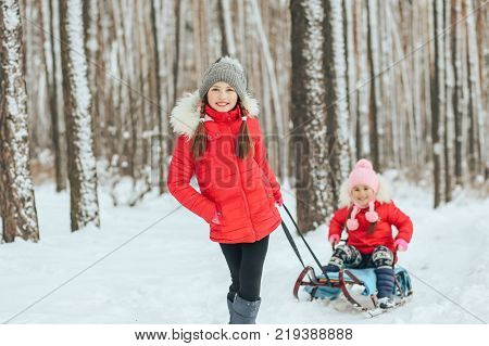 two cute girls sledging in the winter in the woods
