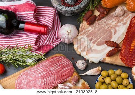Set of different Spanish appetizer, like fuet, jamon, chorizo, bacon and lomo embuchado with a red wine and olives.