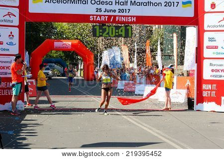 ODESSA UKRAINE - 25 JUN 2017: Excited female runner crossing the finshline of a marathon. Marathon winner woman at finish. Happy marathon runner finish line.