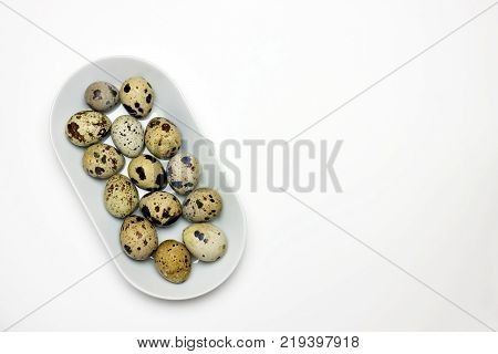 An overhead photo of some uncooked quail eggs in white porcelain plat. Eggs photo from above. Easter background