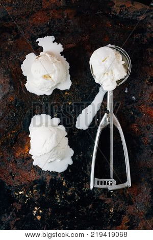 Melted ice cream in metal ice cream scooper over black rustic table