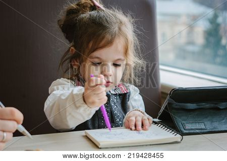 Little kid girl writing or drawing with pen in scetch book.